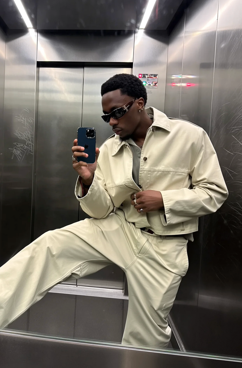 Person taking a mirror selfie in an elevator wearing a beige outfit.