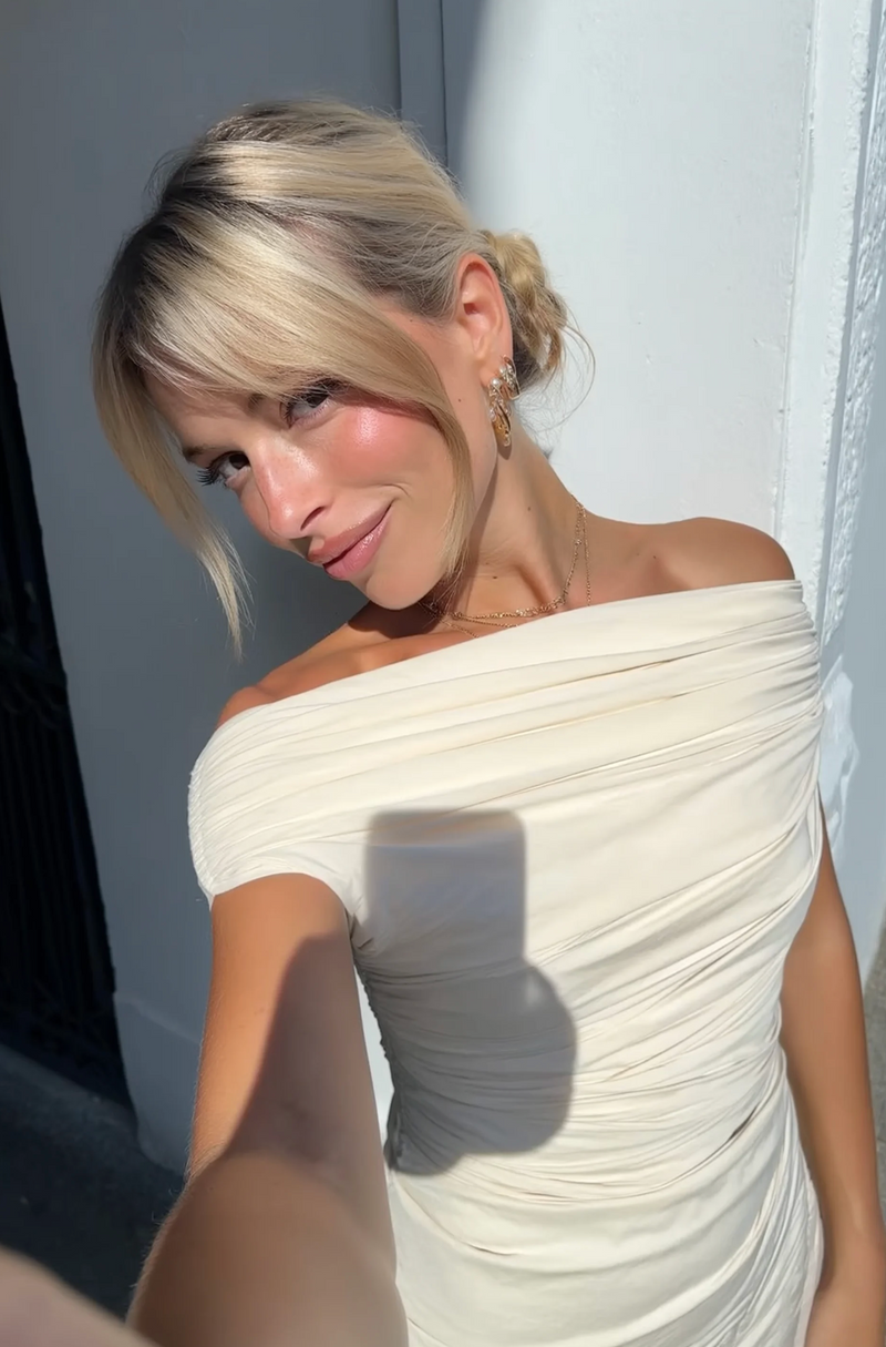 Woman in a white off-shoulder dress taking a selfie.