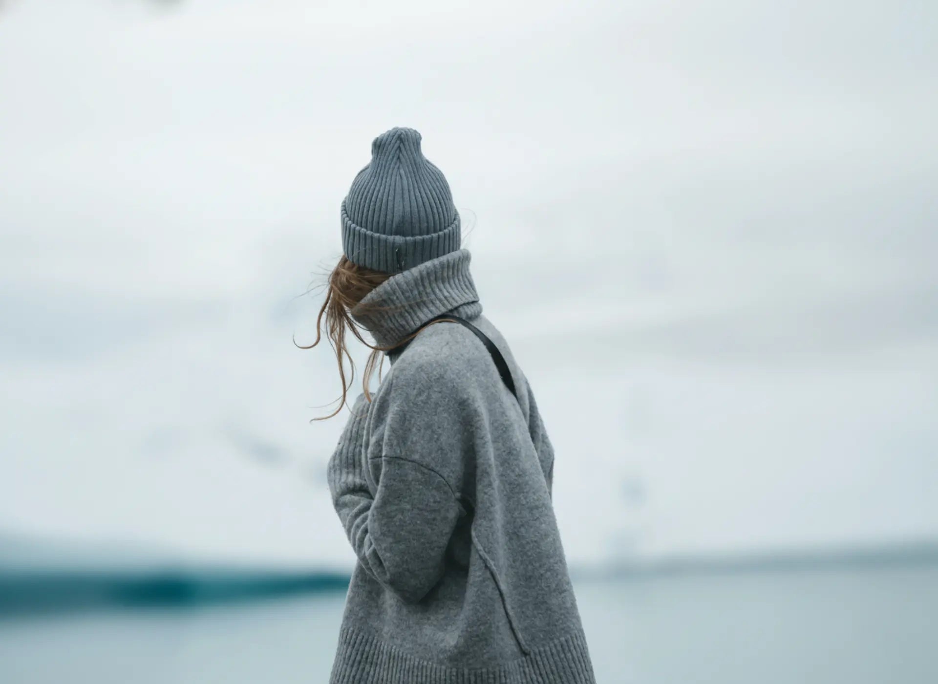 Person wearing a gray sweater and beanie standing in a snowy landscape