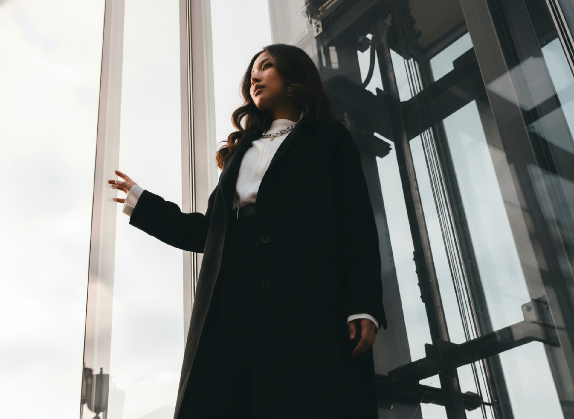 Woman in a black coat standing in front of large windows