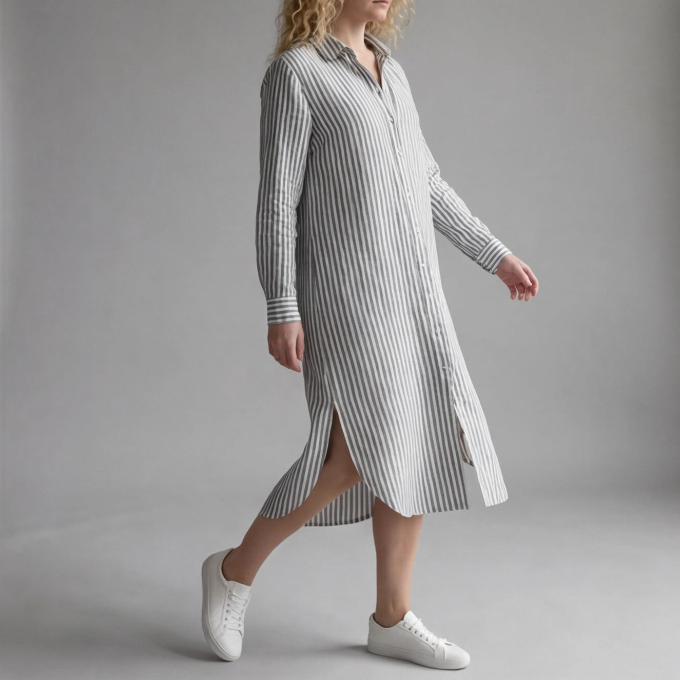 Woman wearing a long striped dress with white sneakers on a gray background