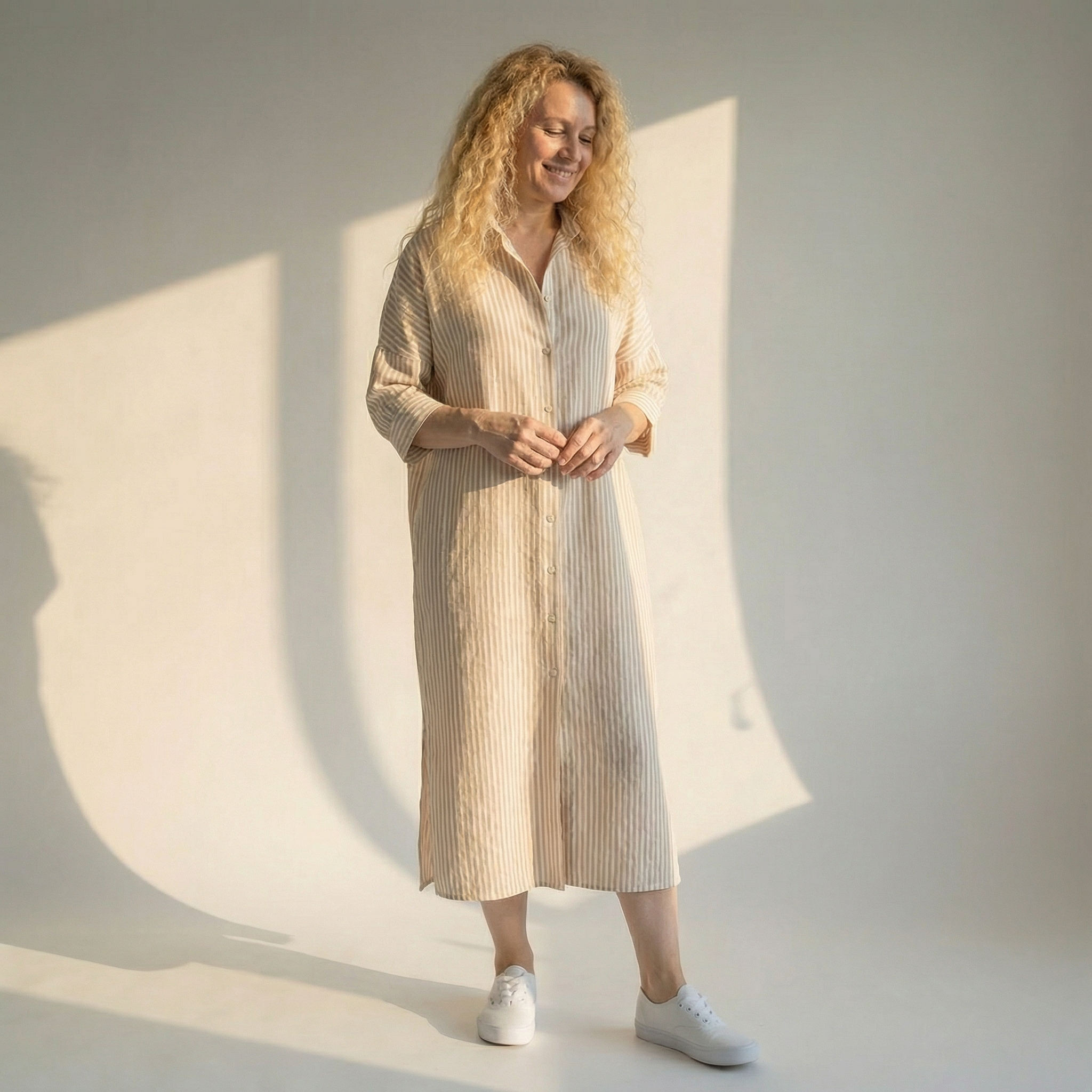 Woman wearing a long, light-colored dress standing in a softly lit room.