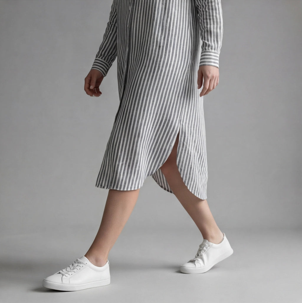 Person wearing a striped dress and white sneakers on a gray background