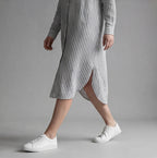 Person wearing a striped dress and white sneakers on a gray background