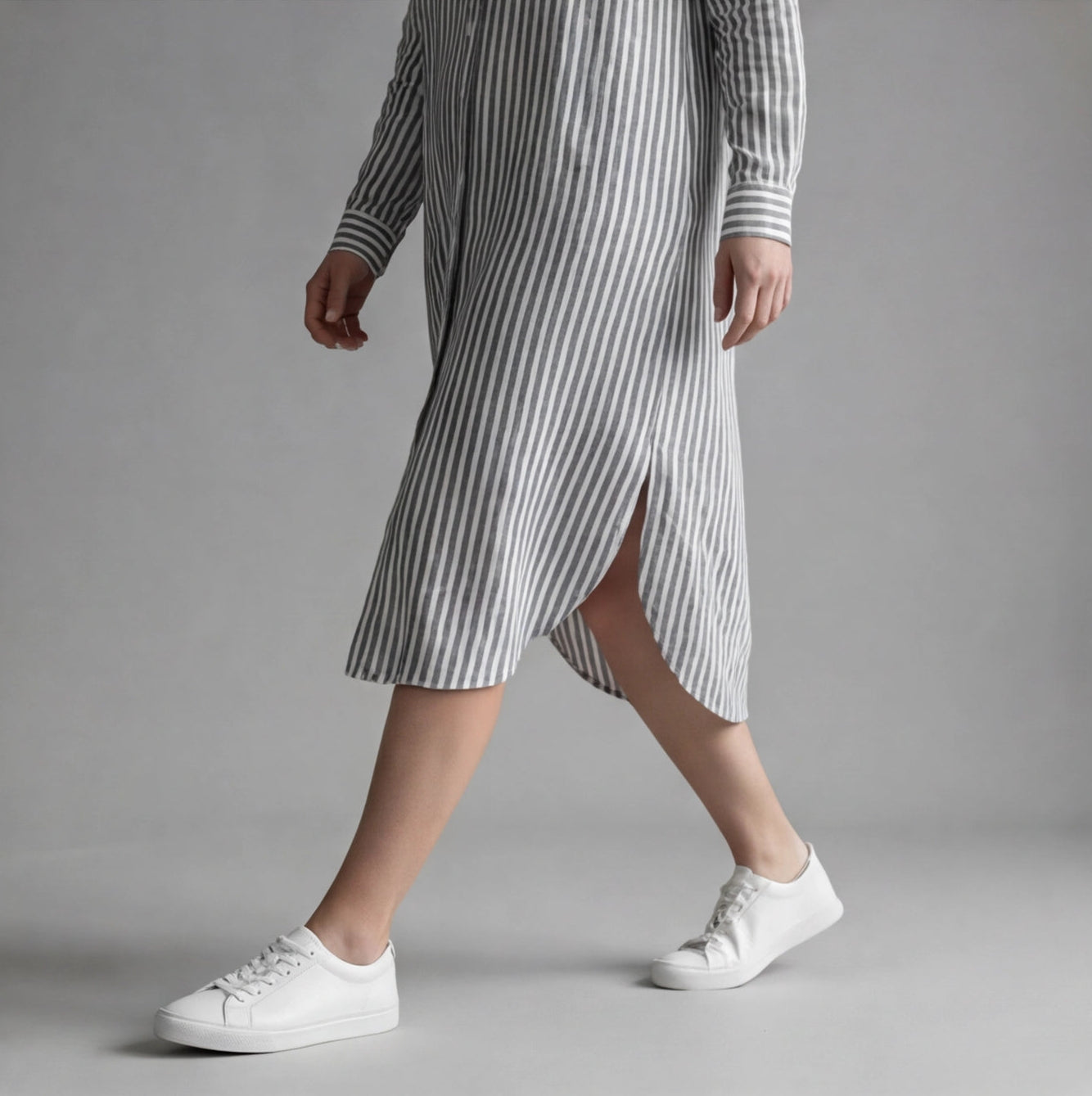 Person wearing a striped dress and white sneakers on a gray background